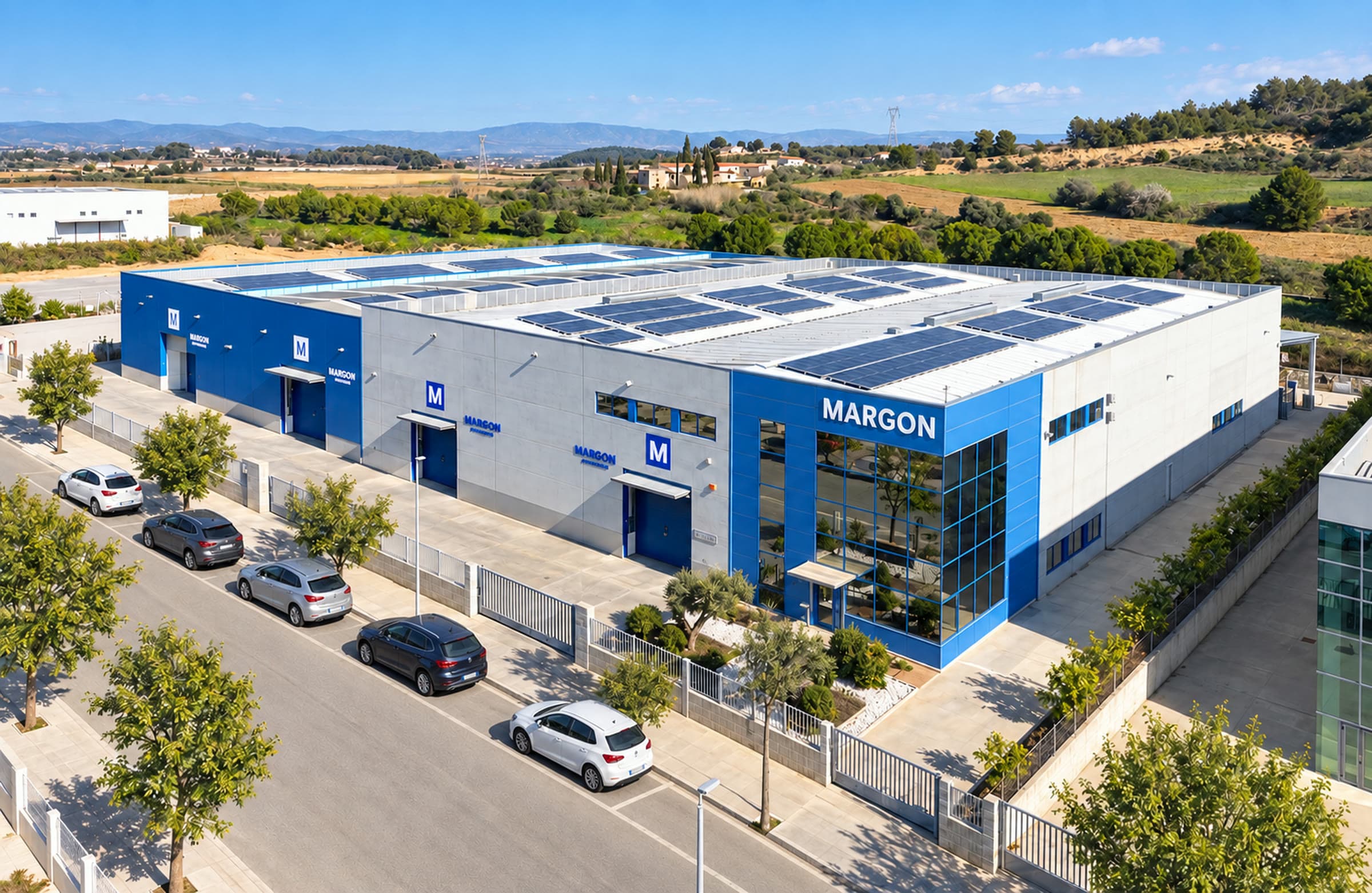 Vista aérea de la planta de Margon en l'Arboç, con la fachada azul corporativa y placas solares en cubierta.